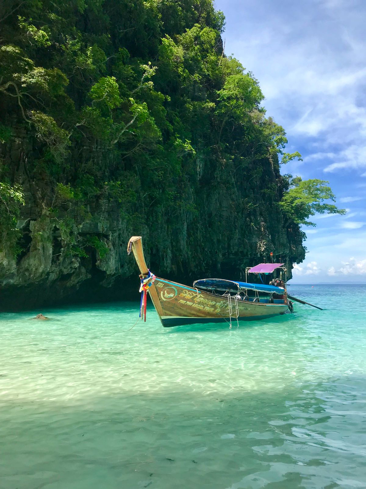 A traditional long-tail boat in clear turquoise waters with lush green cliffs in the background.