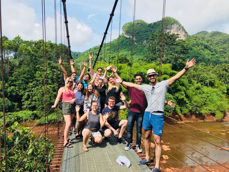 Group of people posing on a suspension bridge in a lush, green landscape.