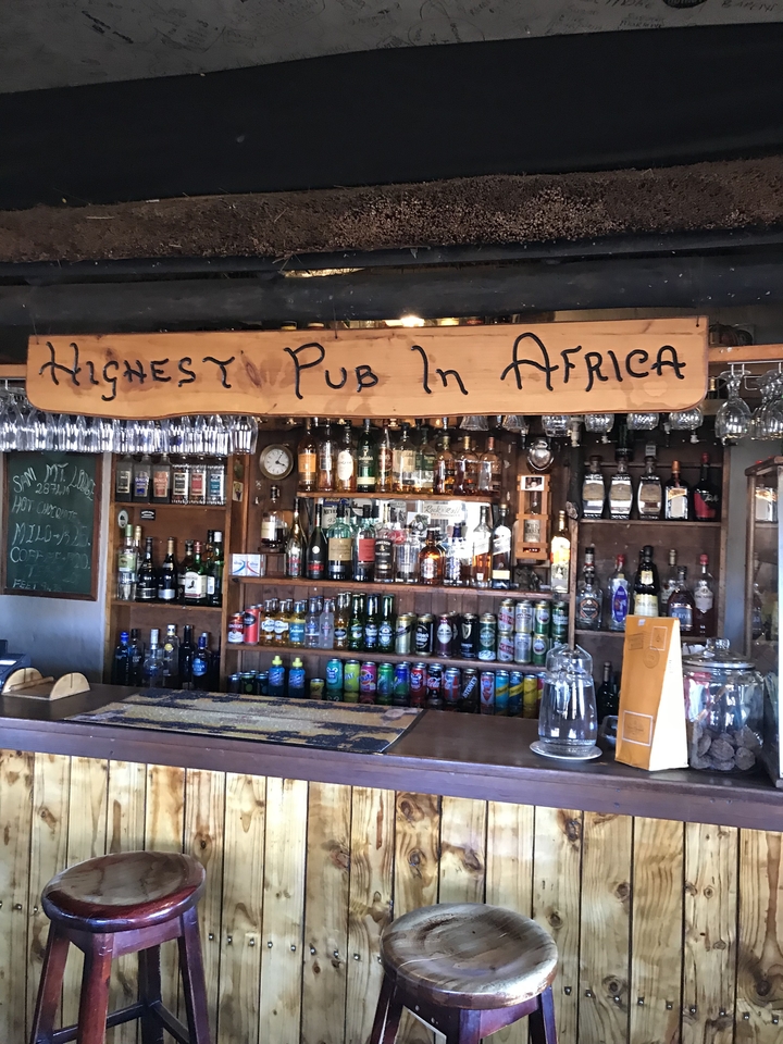 Intérieur du bar avec un assortiment de boissons et l'enseigne du "plus haut pub d'Afrique".