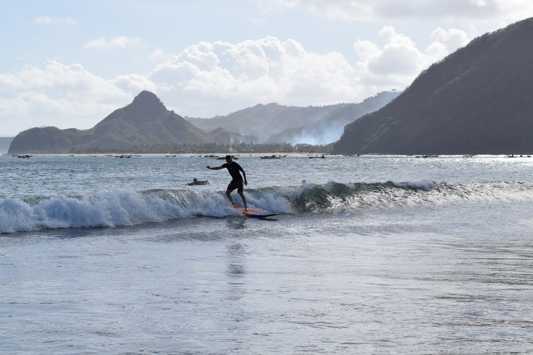 Person surfing on a wave with mountains in the background.