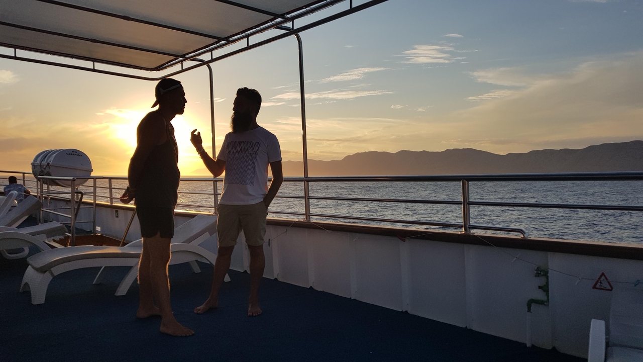 Two people talking on a boat at sunset.