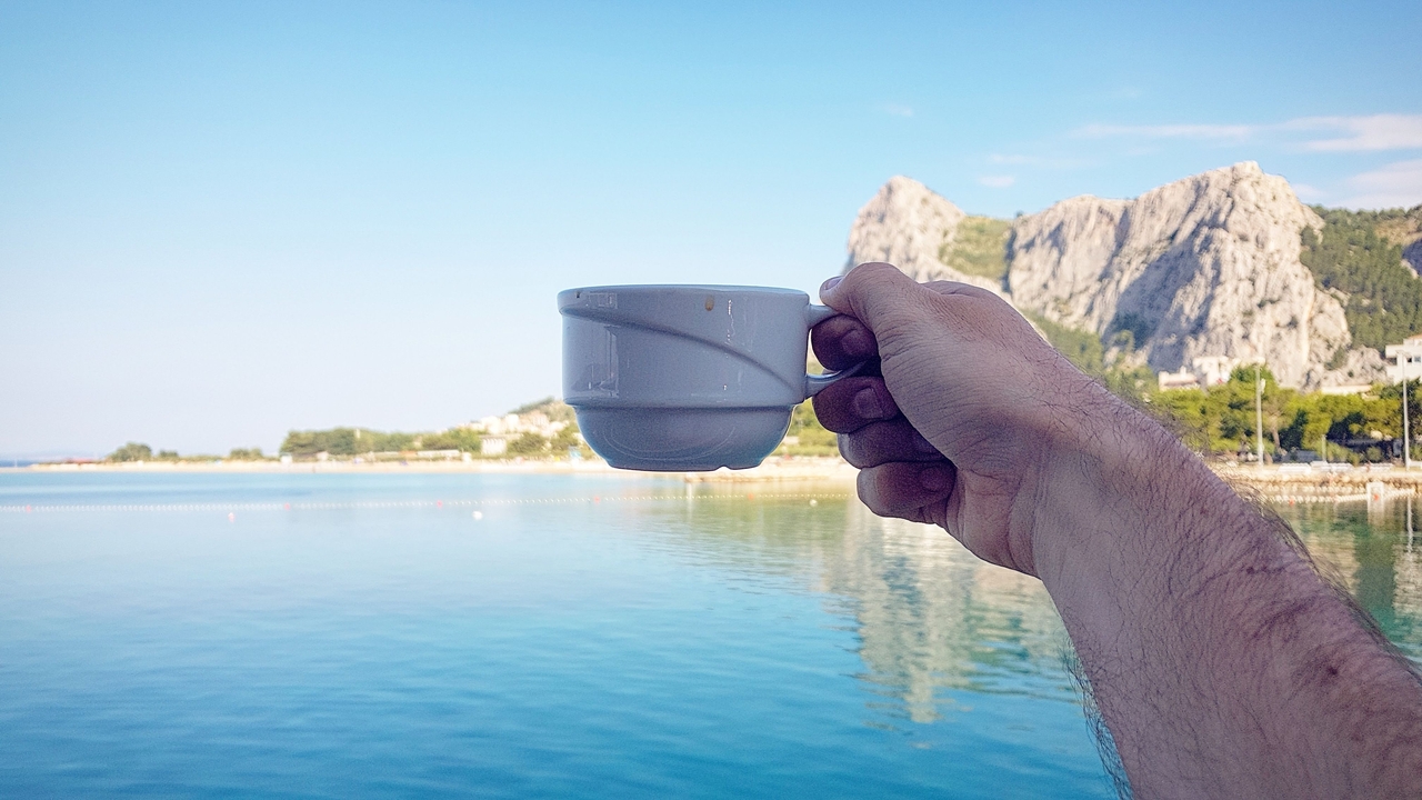 A hand holding a cup with a coastal view in the background.