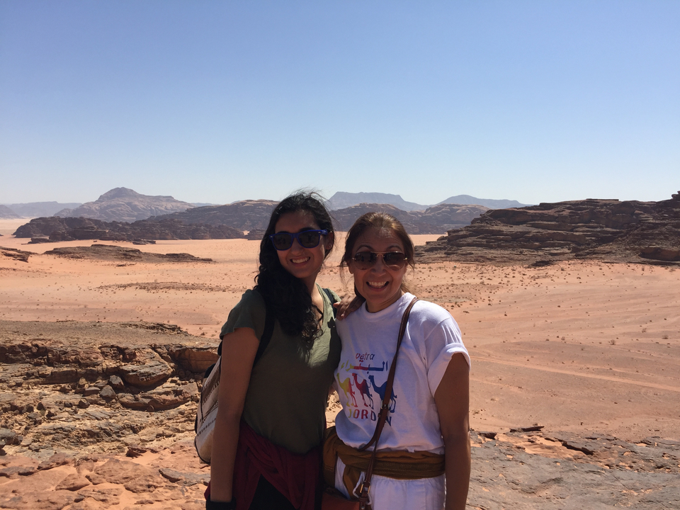 Two women smiling in a desert landscape with rocky hills in the distance.