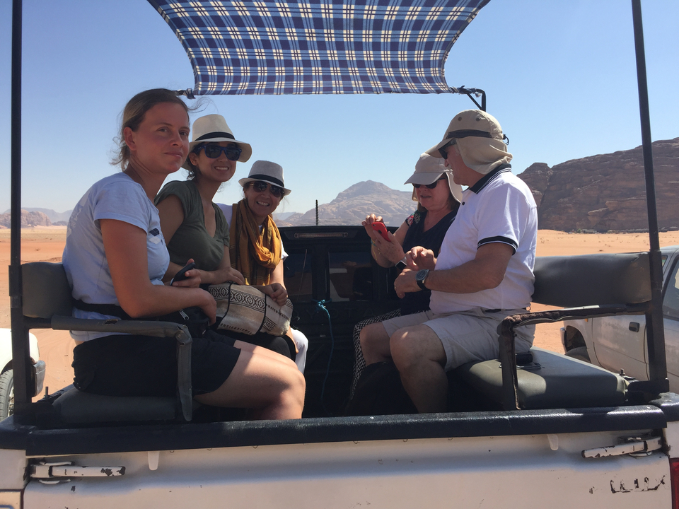 Group of people sitting in a jeep on a desert tour with rocky hills in the distance.