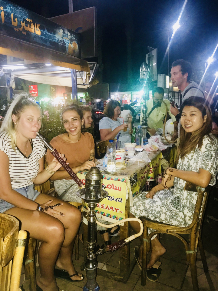 Group of friends enjoying shisha and food at an outdoor night café.