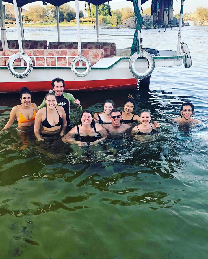 Large group of travellers smiling while swimming beside a boat in a river.