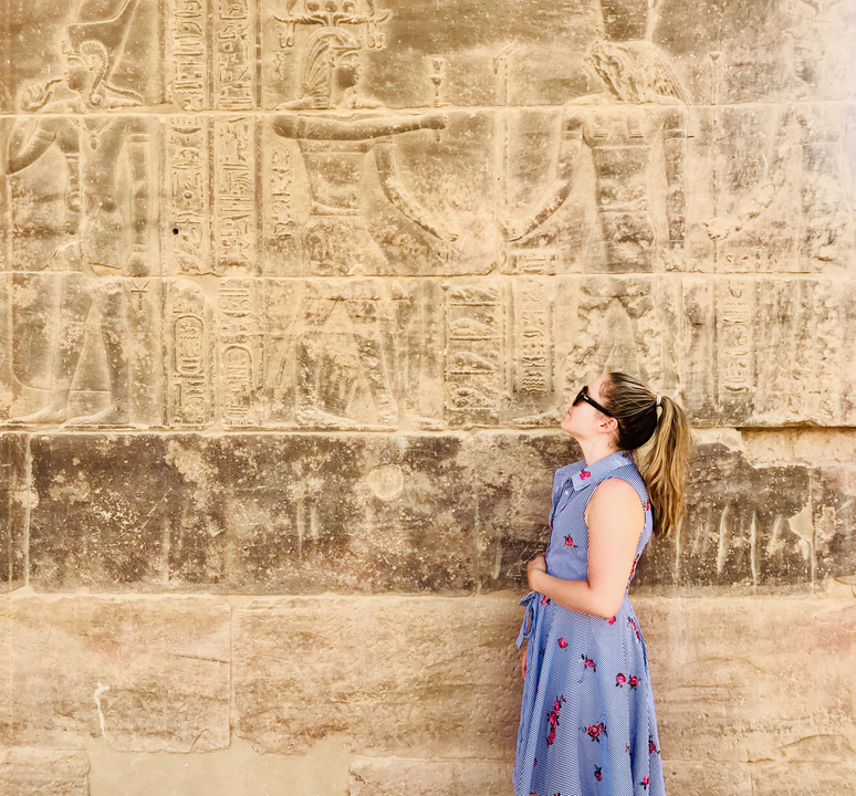 Woman admiring ancient Egyptian relief carvings on a sandstone wall.