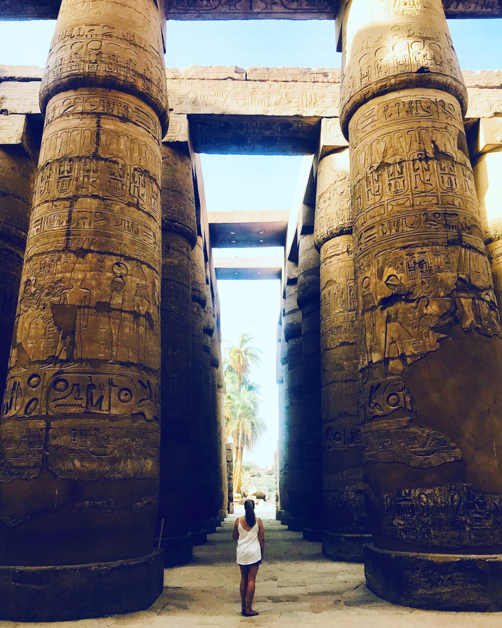 Ornately carved stone columns leading toward sunlight in an ancient temple.