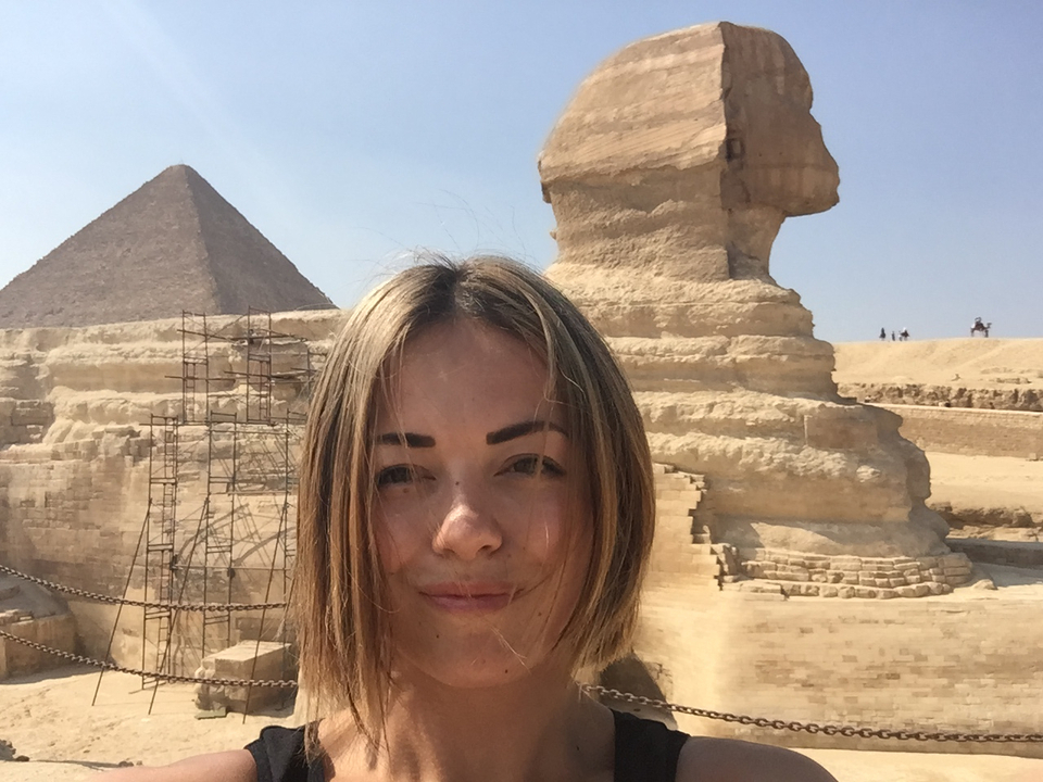 Person taking a selfie with the Sphinx and a pyramid in the background.
