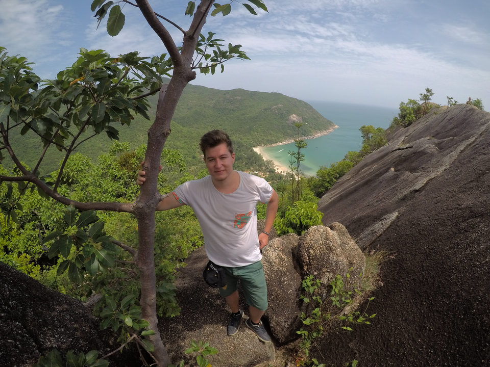Person posing on a mountain with a scenic view of the beach below.