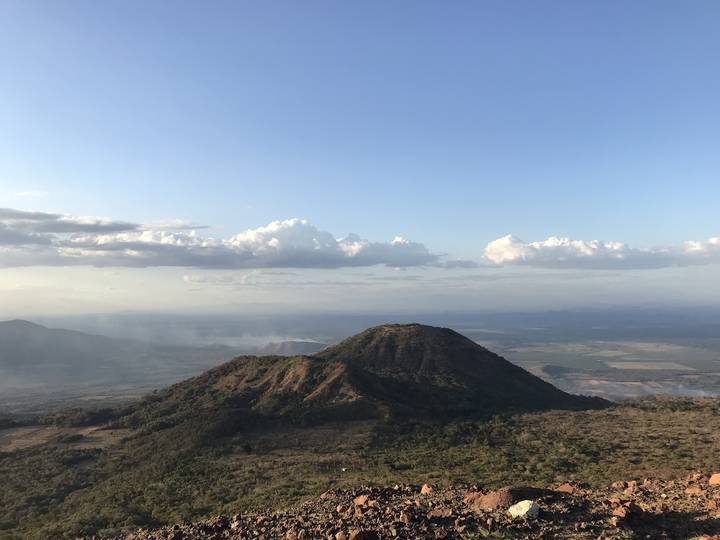 Clear daytime view of a hilltop and distant landscape with clouds overhead.