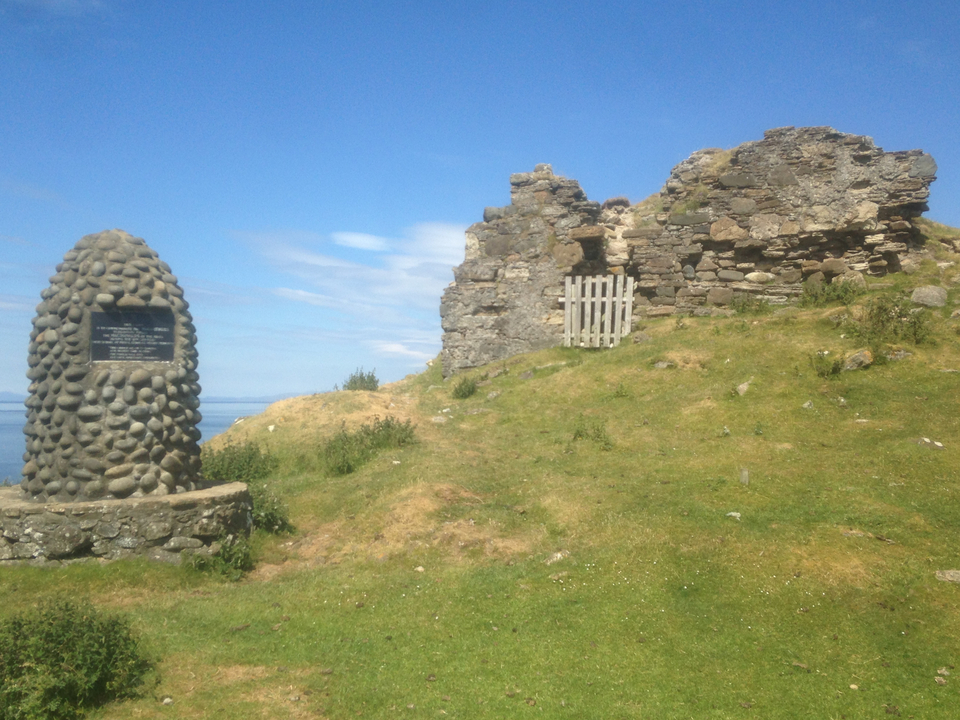 Ruins of a stone structure next to a commemorative stone with a plaque.