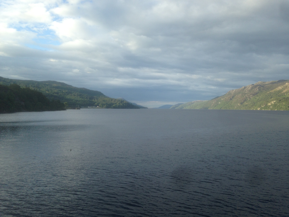 A scenic view of a large lake surrounded by hills under a cloudy sky.