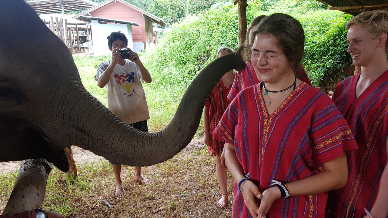 Personne souriante tandis qu'un éléphant touche son épaule avec sa trompe.