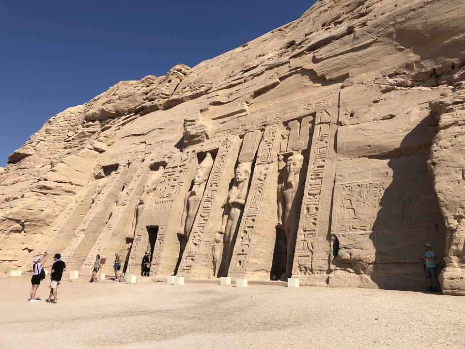 Tourists admiring statues and carvings on an ancient Egyptian temple facade.