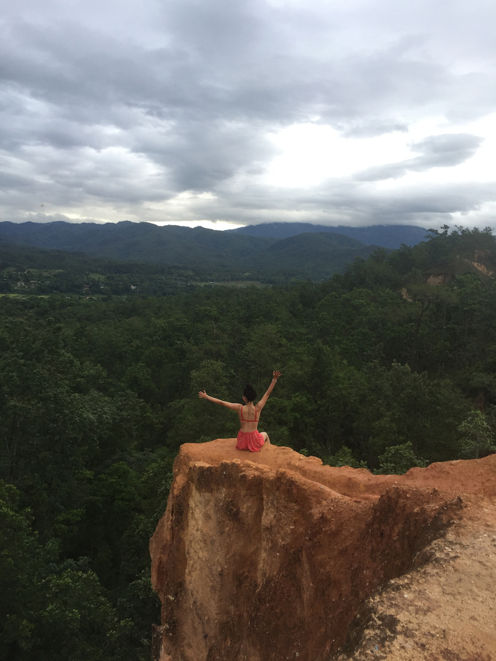 Woman sitting on an edge with forest and mountain range in the backdrop.