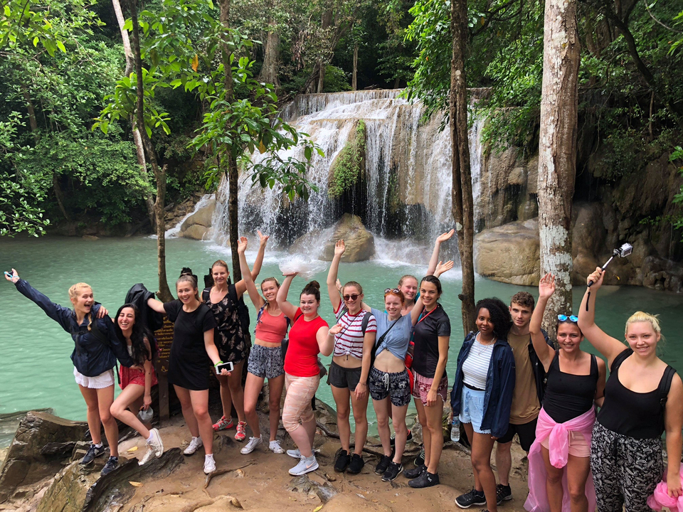 Group posing in front of a waterfall in a lush setting.