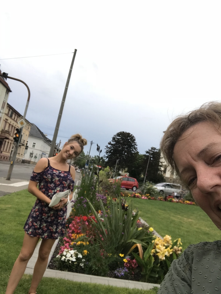 Deux femmes souriantes avec des fleurs et une route en arrière-plan.