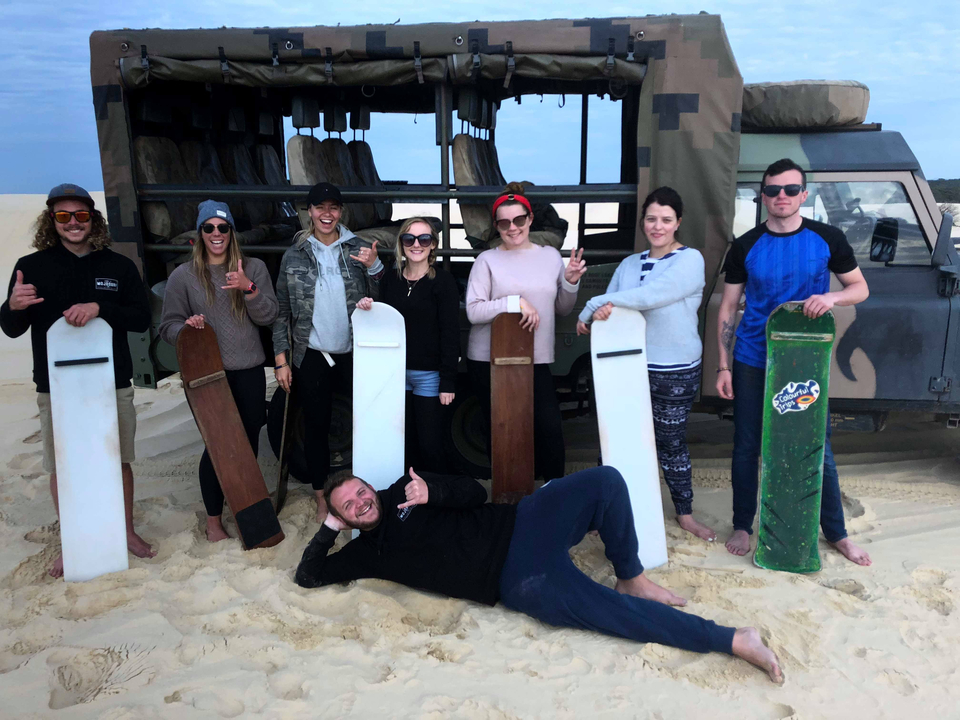 Group of people with sandboards on dunes.