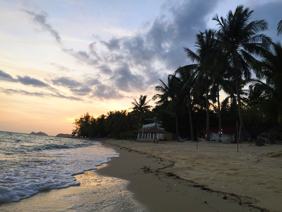 Beach at sunset with palm trees and a distant islet.