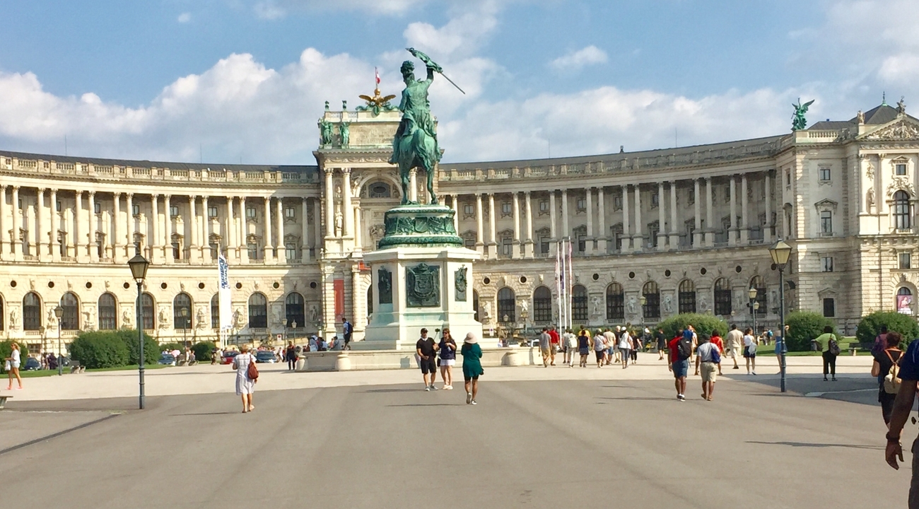 Statue and large historical building with tourists walking around.