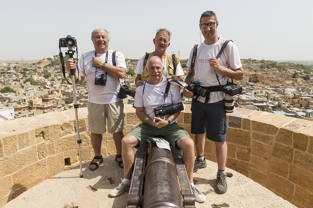 Quatre hommes avec des appareils photo posent au sommet d'un mur de fort surplombant une ville.