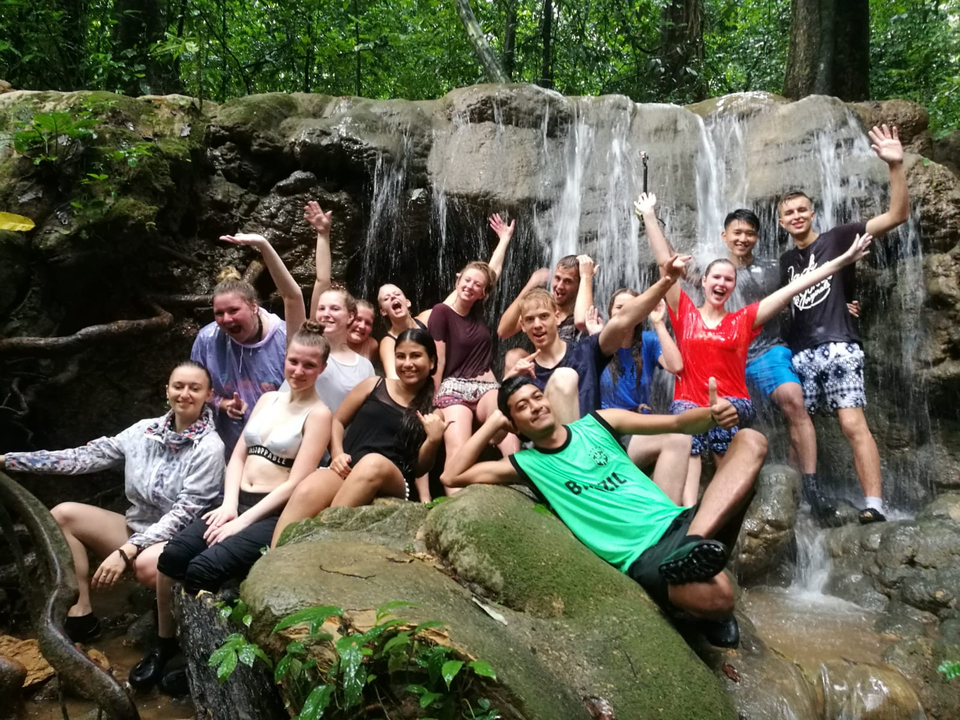 Group of people posing by a waterfall, looking excited.