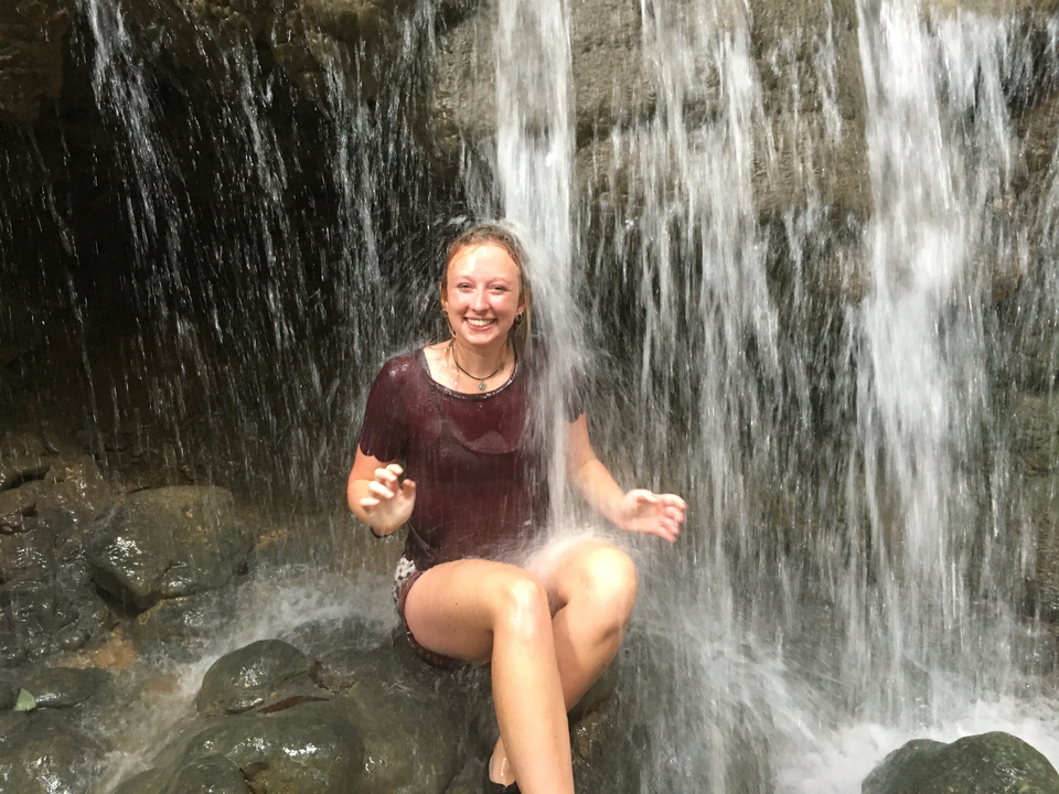 Girl sitting under a waterfall, smiling.