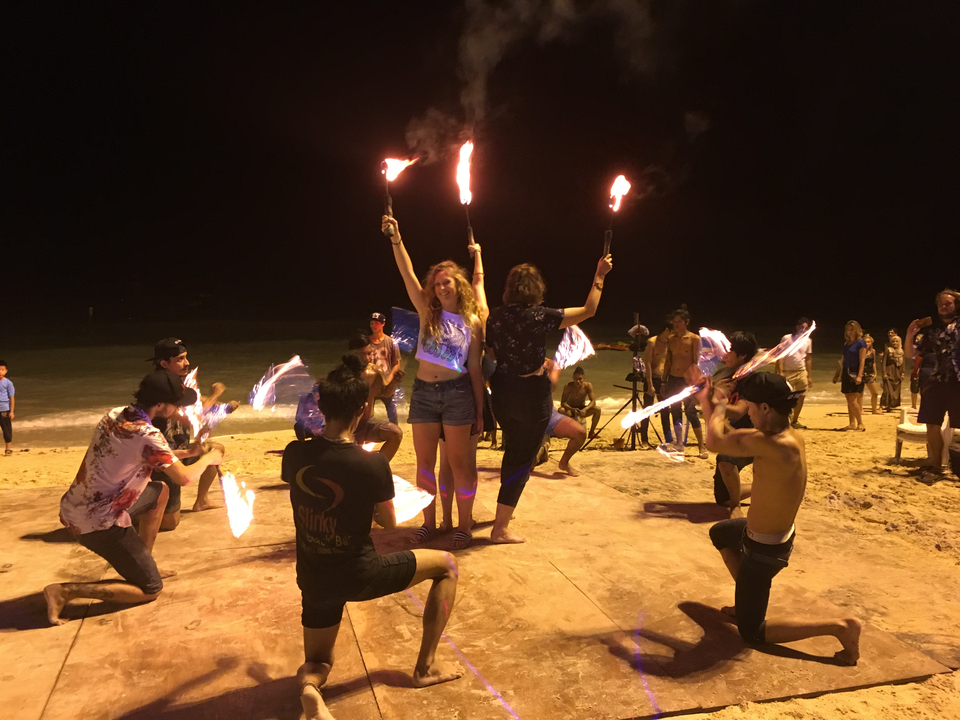 Group fire dancing performance on the beach at night.