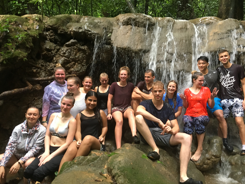 Group sitting by a waterfall in swimwear, smiling.