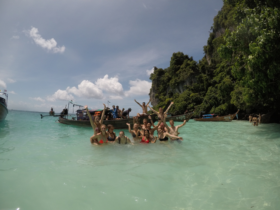 Group posing in the water by longboats at a beach.