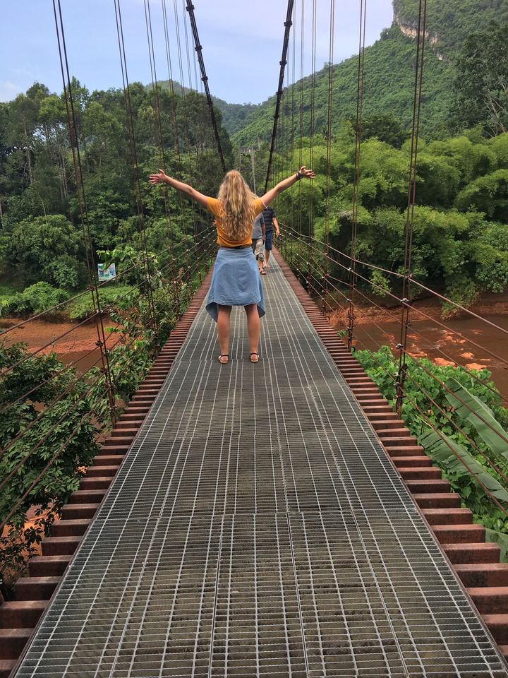 Two people walking on a suspension bridge in a lush environment.