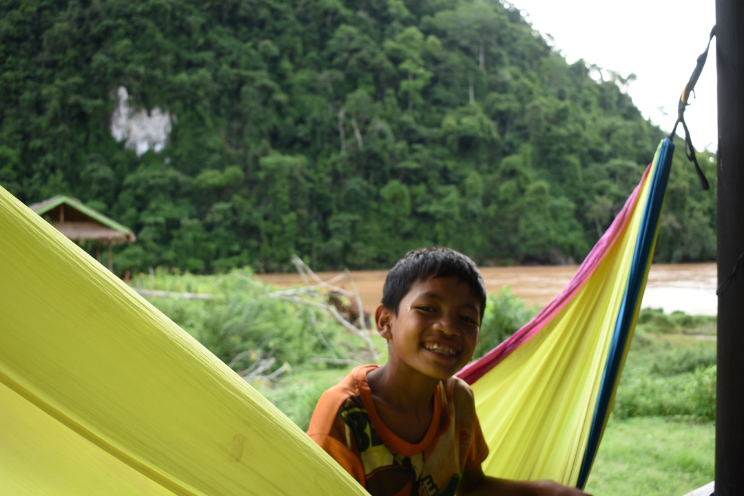 Smiling child sitting in a hammock by a river.