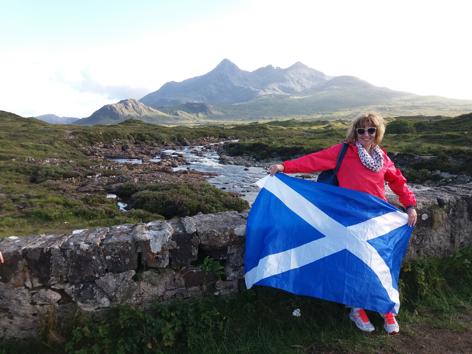 Woman holding a Scottish flag in front of a scenic mountain landscape.