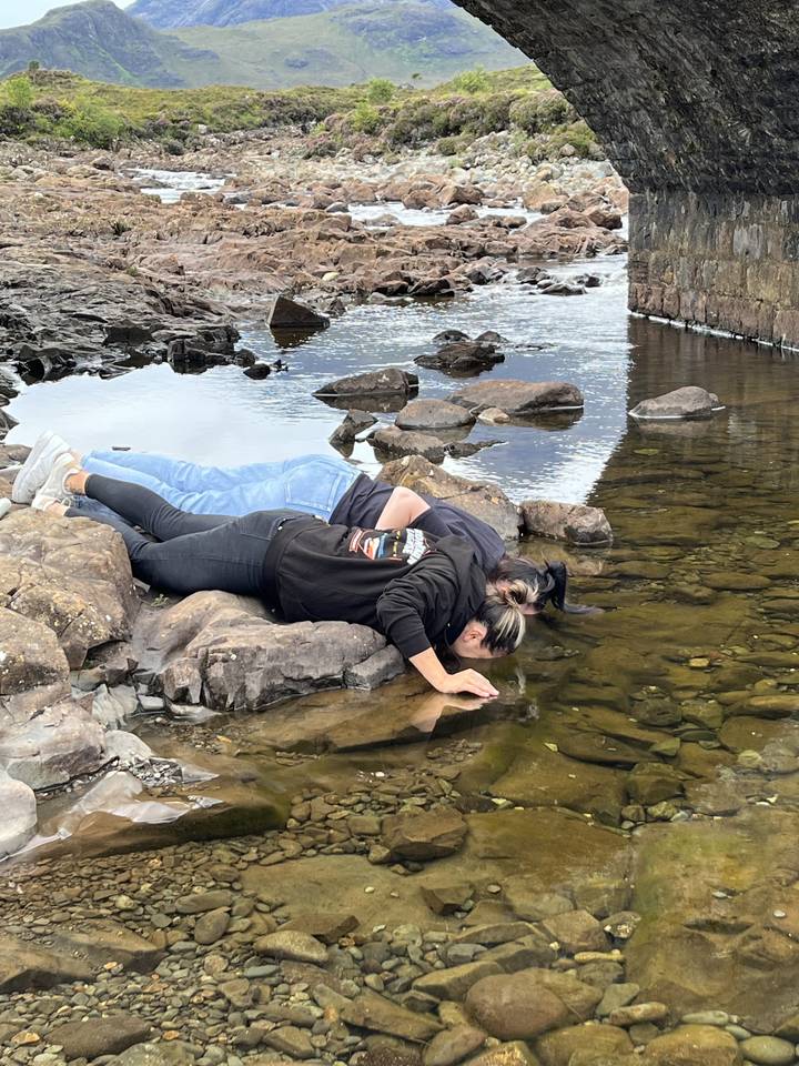 Two people exploring a rocky stream under a bridge.