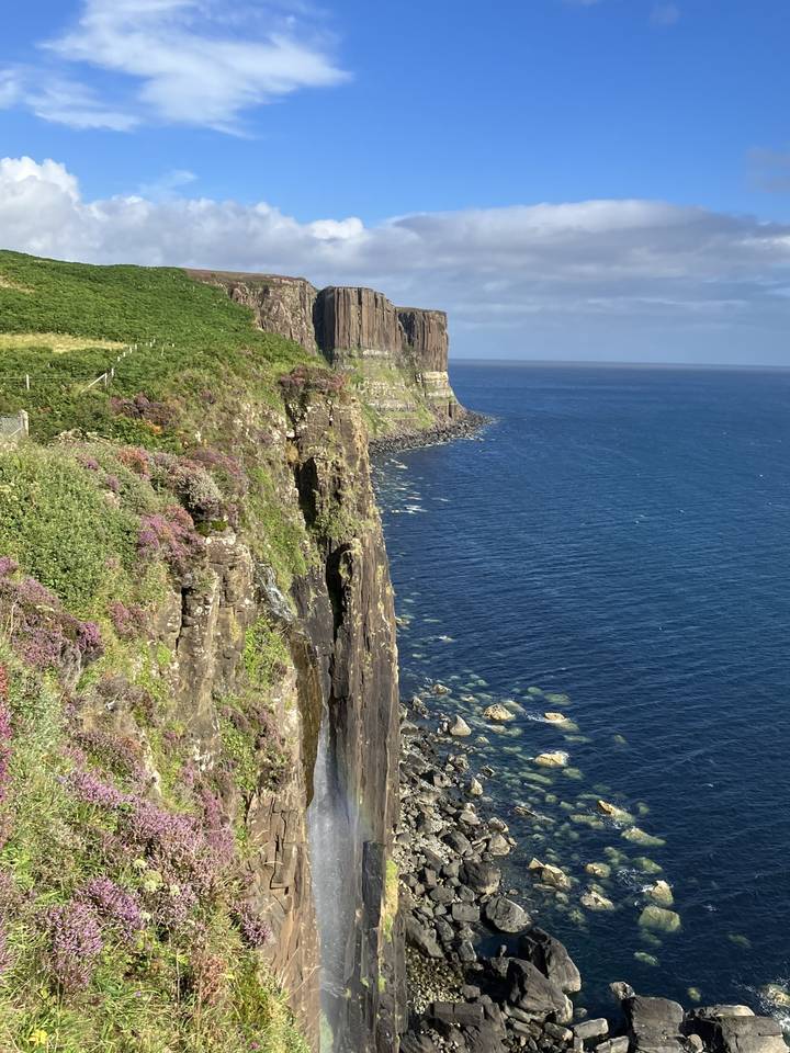 Cliffs with a waterfall leading into the ocean under a blue sky.