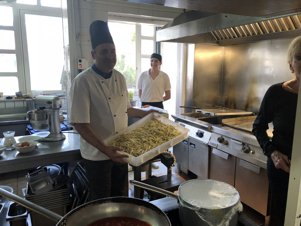 Chef présentant un plateau de pâtes dans une cuisine.