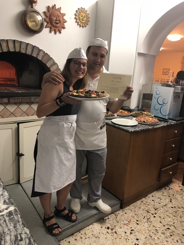 Deux personnes tenant une pizza et un certificat dans une cuisine.