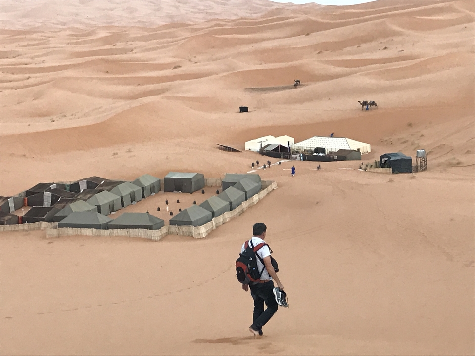 A desert camp with tents and a person walking in the sand dunes.