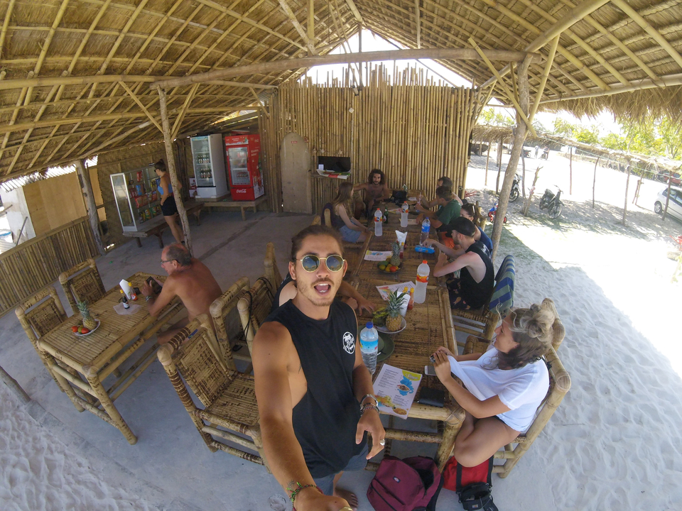 A group of people sitting at a beachside hut with bamboo furniture.