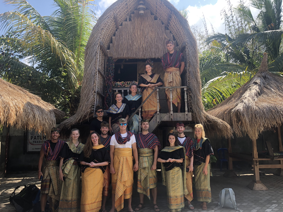 A group wearing traditional clothing in front of a thatched building.
