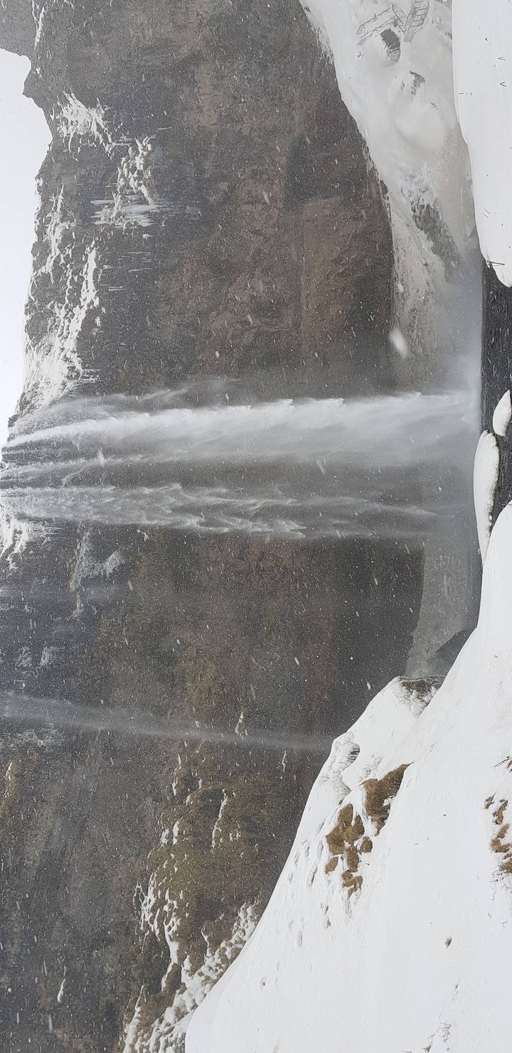 Waterfall cascading over a rocky cliff with snow around.