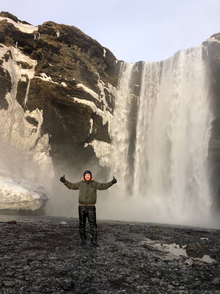 Person standing joyfully in front of a large waterfall.
