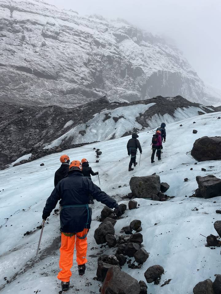 Group of people climbing an icy slope with helmets and gear.