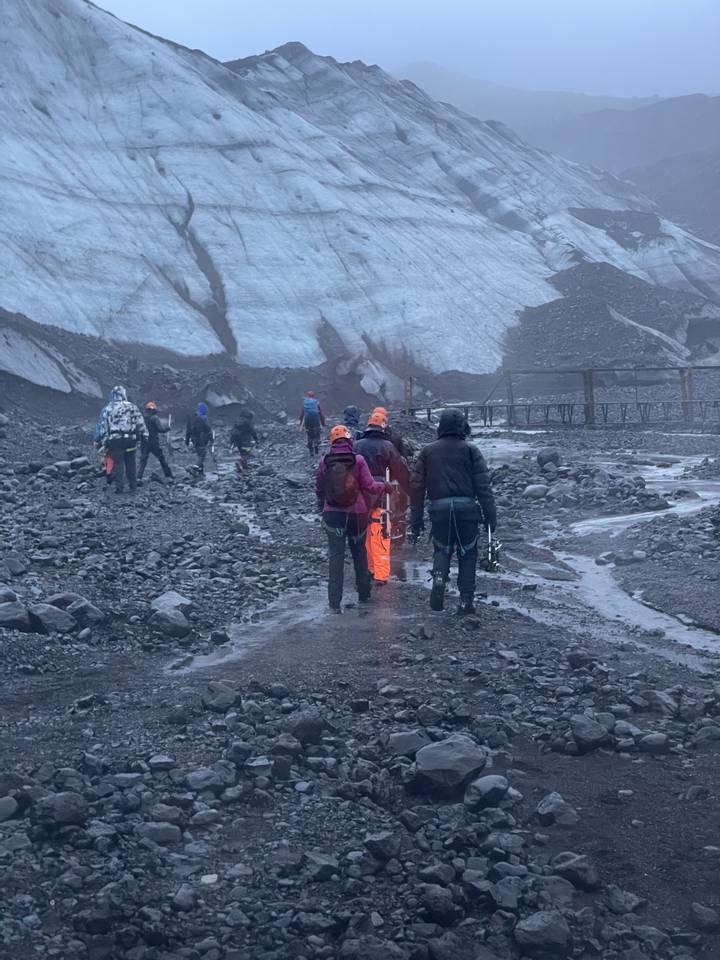 Group walking on rocky path next to glacier and ice.