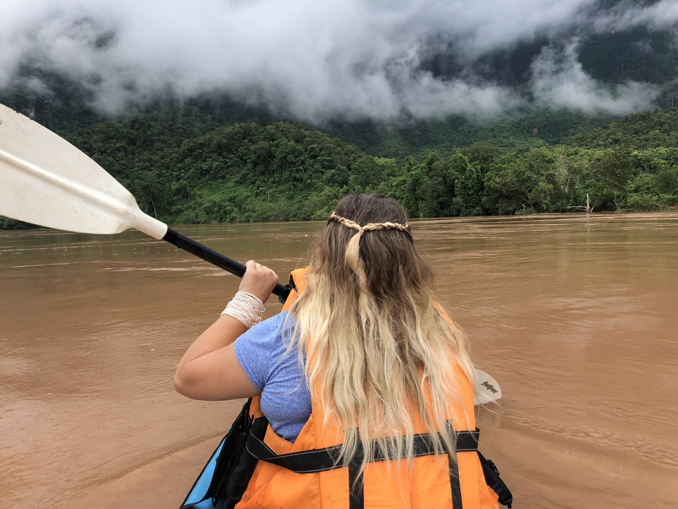Person kayaking on a wide river with lush hills in the background.