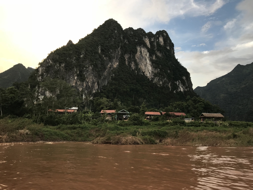 Steep rocky mountain with houses along the shore of a river.