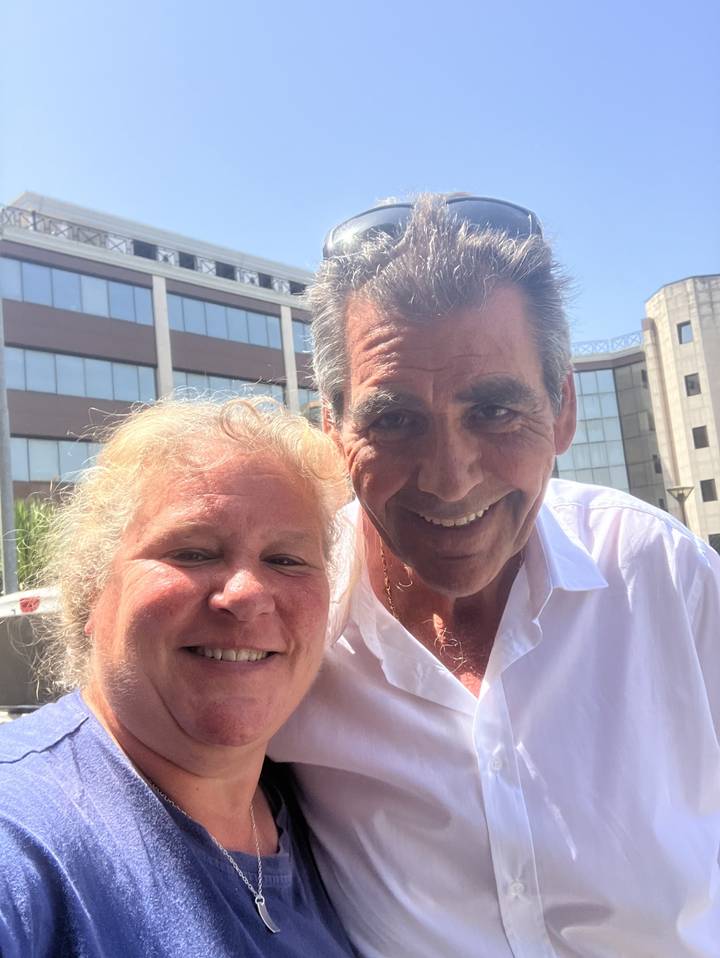 Selfie de deux personnes à l'extérieur avec un bâtiment en arrière-plan.