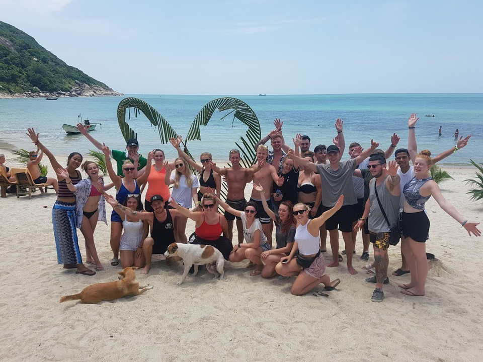 A group of friends standing on a beach with their arms raised.
