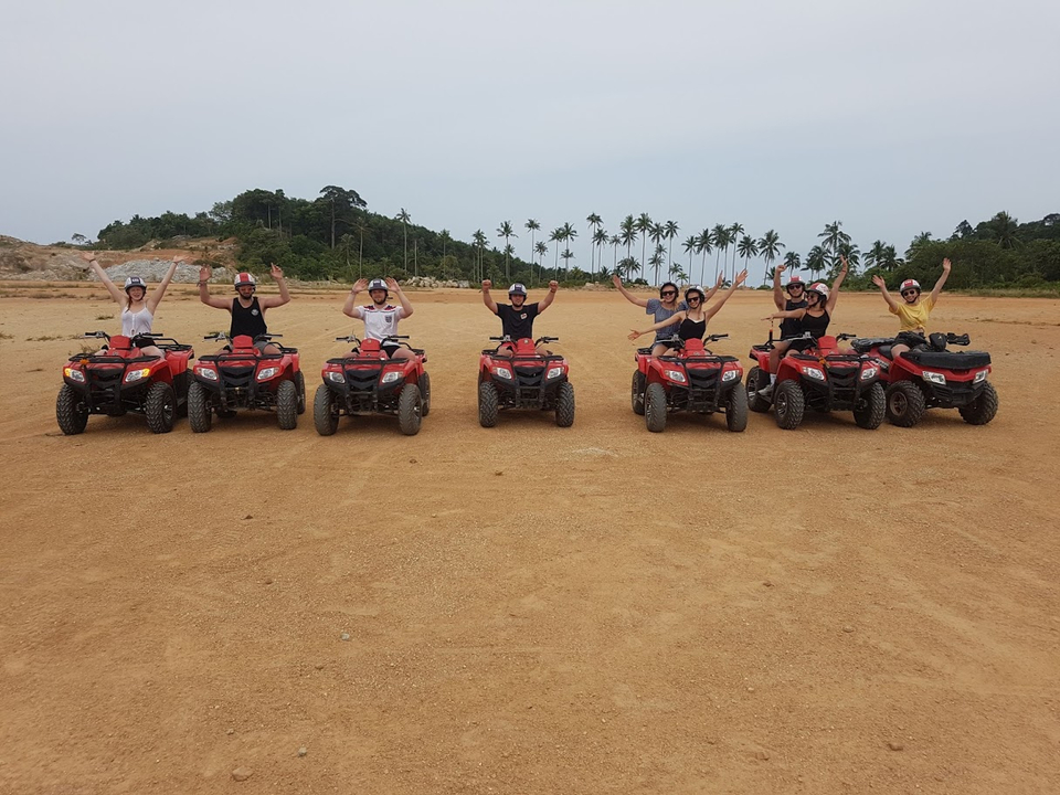 A group of people posing with ATVs on sandy terrain with palm trees.